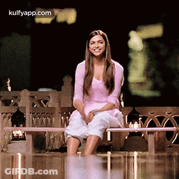 A Woman Is Sitting On A Bench With Her Legs Crossed And Smiling At The Camera . GIF