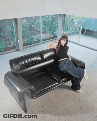 A Woman Is Sitting On A Black Leather Couch With Her Legs Crossed GIF