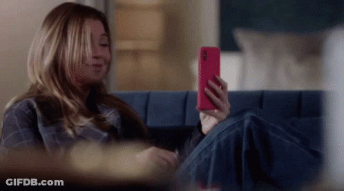 A Woman Is Sitting On A Blue Couch Looking At Her Phone GIF