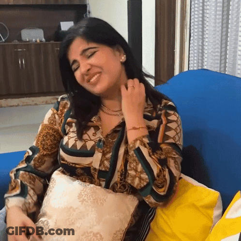 A Woman Is Sitting On A Blue Couch With A Pillow And Smiling GIF
