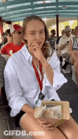 A Woman Is Sitting On A Boat Holding A Box Of Food And Covering Her Mouth . GIF