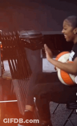 A Woman Is Sitting On A Chair Holding A Basketball And Giving A High Five . GIF