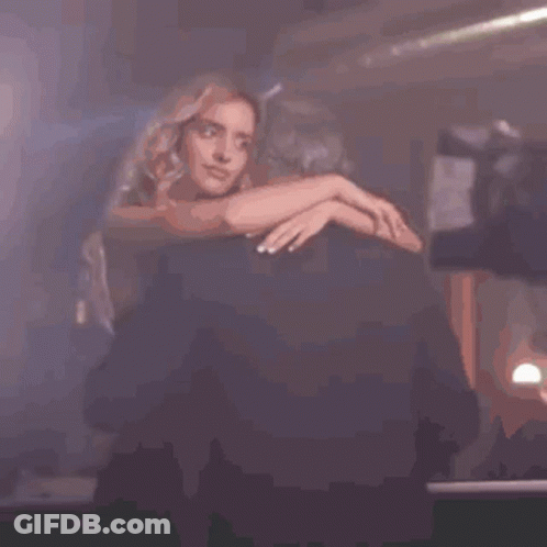A Woman Is Sitting On A Chair In A Dark Room With Her Hands On Her Hips . GIF