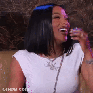 A Woman Is Sitting On A Couch And Laughing While Wearing A White Shirt . GIF