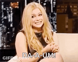 A Woman Is Sitting On A Couch And Smiling While Holding Her Hands Together . GIF