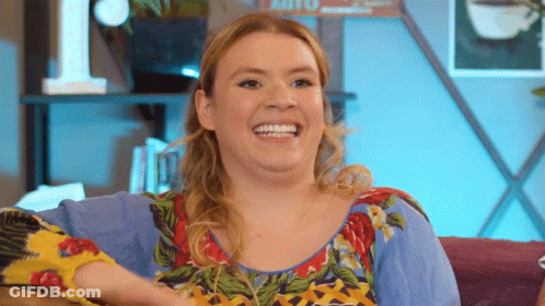 A Woman Is Sitting On A Couch And Smiling While Wearing A Colorful Shirt GIF