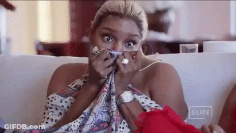 A Woman Is Sitting On A Couch Covering Her Face With A Scarf And A Watch . GIF