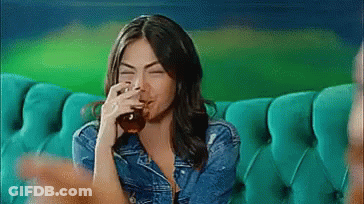 A Woman Is Sitting On A Couch Drinking From A Glass . GIF