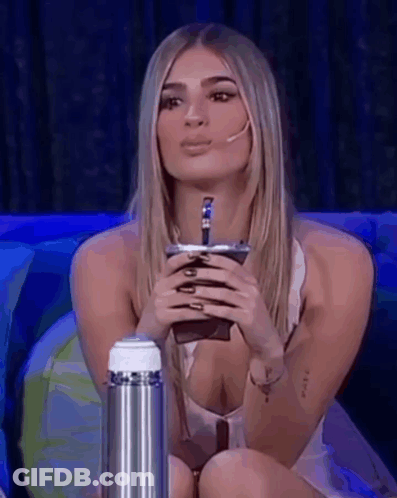 A Woman Is Sitting On A Couch Holding A Cup In Her Hand . GIF