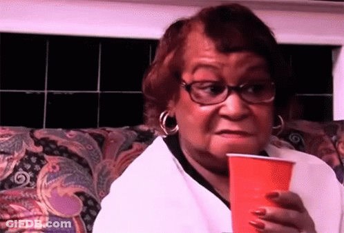 A Woman Is Sitting On A Couch Holding A Red Cup And Making A Funny Face . GIF