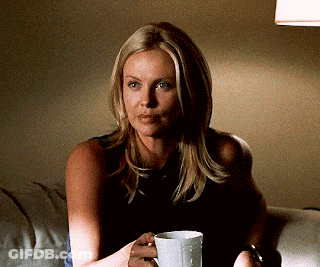 A Woman Is Sitting On A Couch Holding A White Cup GIF