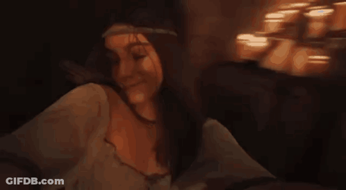 A Woman Is Sitting On A Couch In A Dark Room With Candles In The Background . GIF