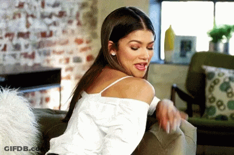 A Woman Is Sitting On A Couch In A Living Room Looking Over Her Shoulder . GIF