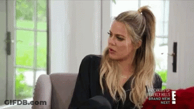 A Woman Is Sitting On A Couch In A Living Room Talking To Someone . GIF
