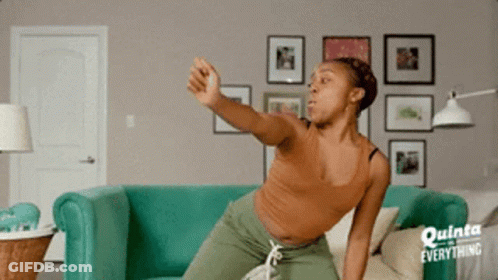 A Woman Is Sitting On A Couch In A Living Room With A Sign That Says Everything GIF