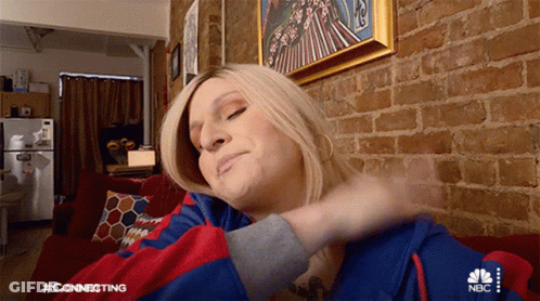 A Woman Is Sitting On A Couch In Front Of A Brick Wall Wearing A Nbc Hoodie GIF