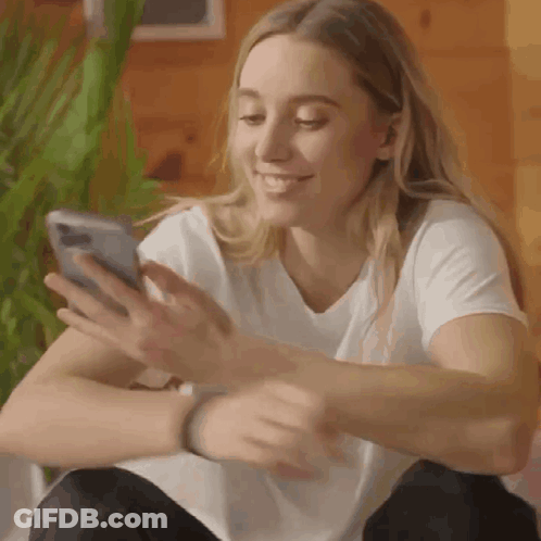 A Woman Is Sitting On A Couch Looking At Her Phone . GIF