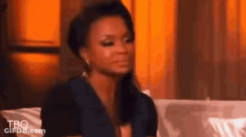 A Woman Is Sitting On A Couch Making A Funny Face And Looking At The Camera . GIF