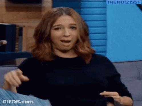A Woman Is Sitting On A Couch Making A Funny Face And Pointing At The Camera . GIF