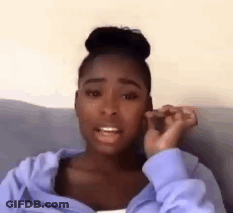 A Woman Is Sitting On A Couch Talking On A Cell Phone While Wearing A Blue Hoodie . GIF