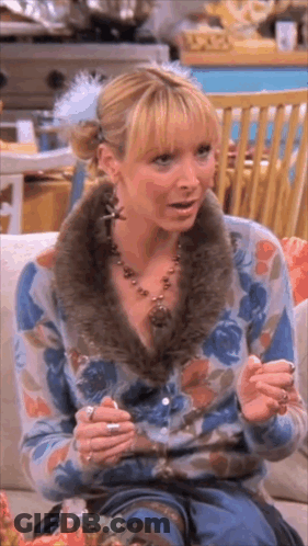 A Woman Is Sitting On A Couch Wearing A Floral Cardigan And A Fur Collar . GIF