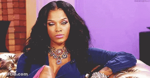 A Woman Is Sitting On A Couch Wearing A Necklace And Bracelets And Making A Funny Face . GIF