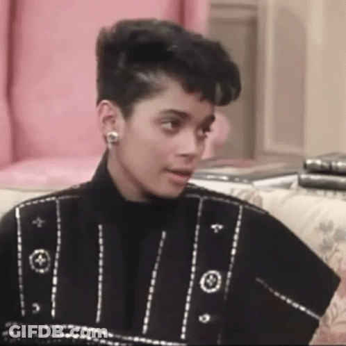 A Woman Is Sitting On A Couch Wearing Earrings And A Black Jacket . GIF