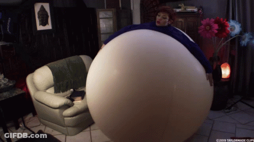 A Woman Is Sitting On A Couch With A Large Balloon Around Her Belly GIF