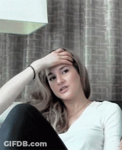 A Woman Is Sitting On A Couch With Her Hand On Her Head GIF