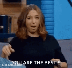 A Woman Is Sitting On A Couch With Her Mouth Open And Pointing At The Camera . GIF