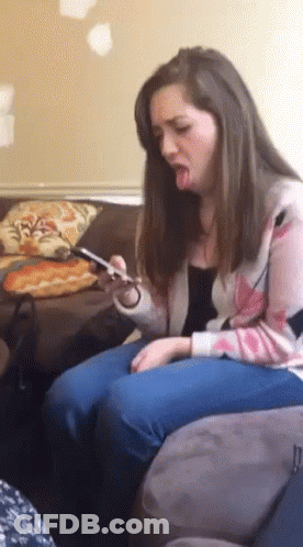 A Woman Is Sitting On A Couch With Her Tongue Out And Looking At Her Phone GIF