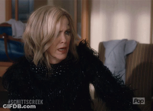 A Woman Is Sitting On A Couch With #Schittscreek Written On The Bottom GIF