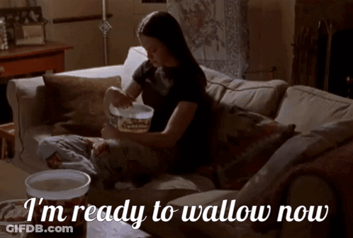 A Woman Is Sitting On A Couch With The Words I 'M Ready To Wallow Now GIF