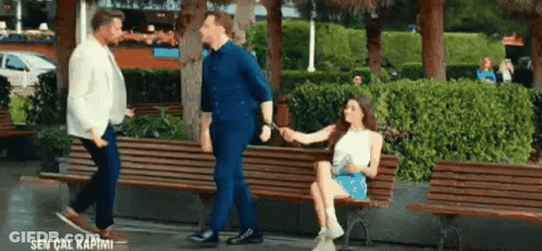 A Woman Is Sitting On A Park Bench Holding Hands With Two Men . GIF
