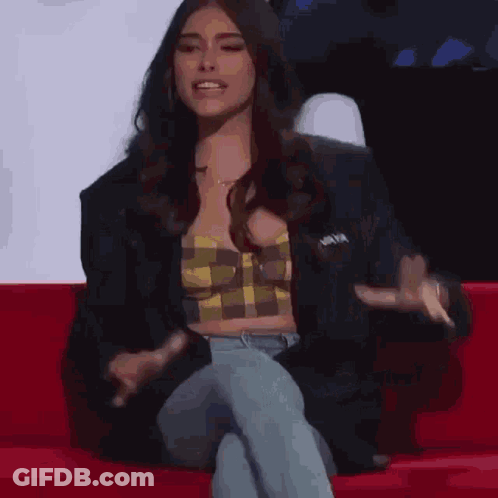 A Woman Is Sitting On A Red Couch With Her Legs Crossed And Talking . GIF