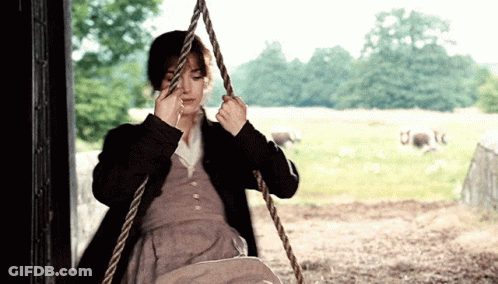 A Woman Is Sitting On A Rope Swing In A Field With Sheep In The Background GIF