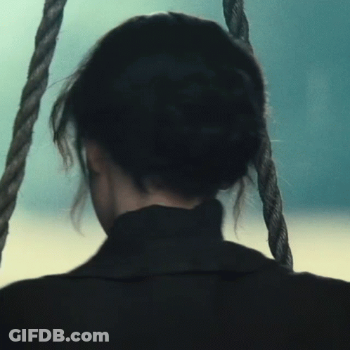 A Woman Is Sitting On A Rope Swing Looking Out Over The Ocean GIF
