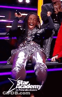 A Woman Is Sitting On A Stage In A Star Academy Le Prime Des Anciens Show And Laughing . GIF