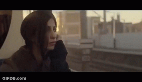 A Woman Is Sitting On A Train Looking Out The Window At The City . GIF