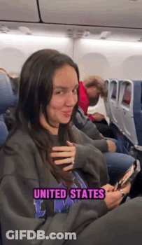 A Woman Is Sitting On An Airplane Wearing A Sweatshirt That Says United States On It . GIF