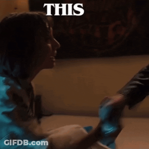 A Woman Is Sitting On The Floor With A Man Holding Her Hand And A Sign That Says This . GIF