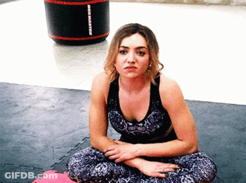 A Woman Is Sitting On The Floor With Her Legs Crossed In A Gym . GIF