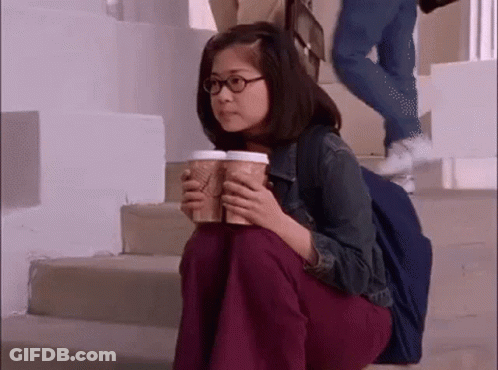 A Woman Is Sitting On The Stairs Holding Two Coffee Cups GIF