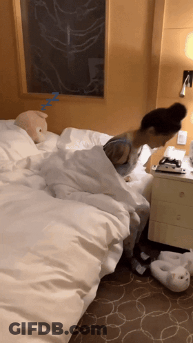A Woman Is Sleeping On A Bed Next To A Nightstand With A Stuffed Animal On It GIF