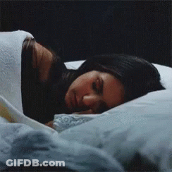 A Woman Is Sleeping On A Bed With A White Blanket GIF