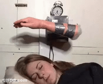 A Woman Is Sleeping With Her Eyes Closed And A Clock On The Wall Above Her Head GIF