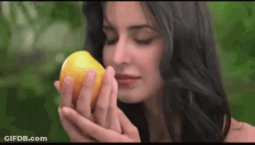 A Woman Is Smelling A Lemon In Her Hand . GIF