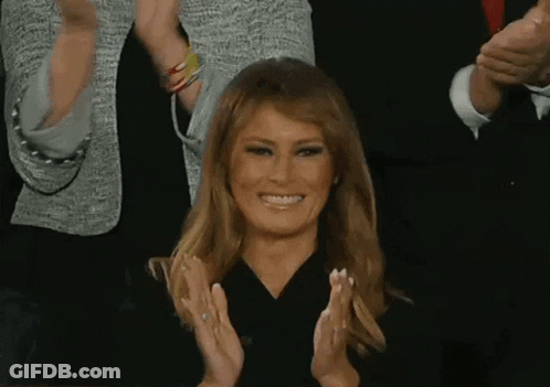 A Woman Is Smiling And Clapping Her Hands In Front Of A Crowd Of People . GIF