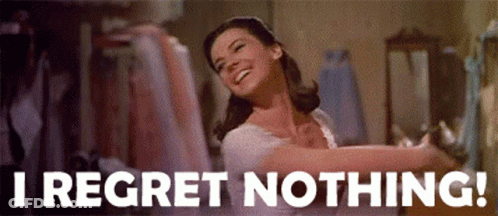 A Woman Is Smiling And Dancing In A Room With The Words `` I Regret Nothing '' Written On The Bottom . GIF