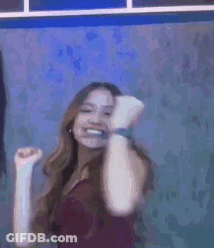 A Woman Is Smiling And Dancing In Front Of A Blue Wall . GIF